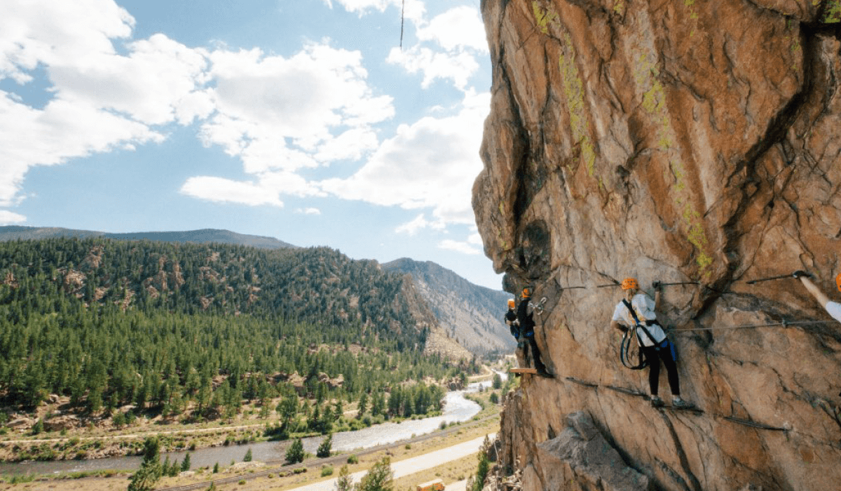 Guests on a cliffside via ferrata route in Buena Vista with the arkansas river and the mountains in the background