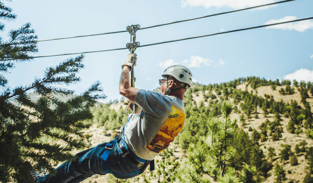 Older male ziplining with mountains in the background