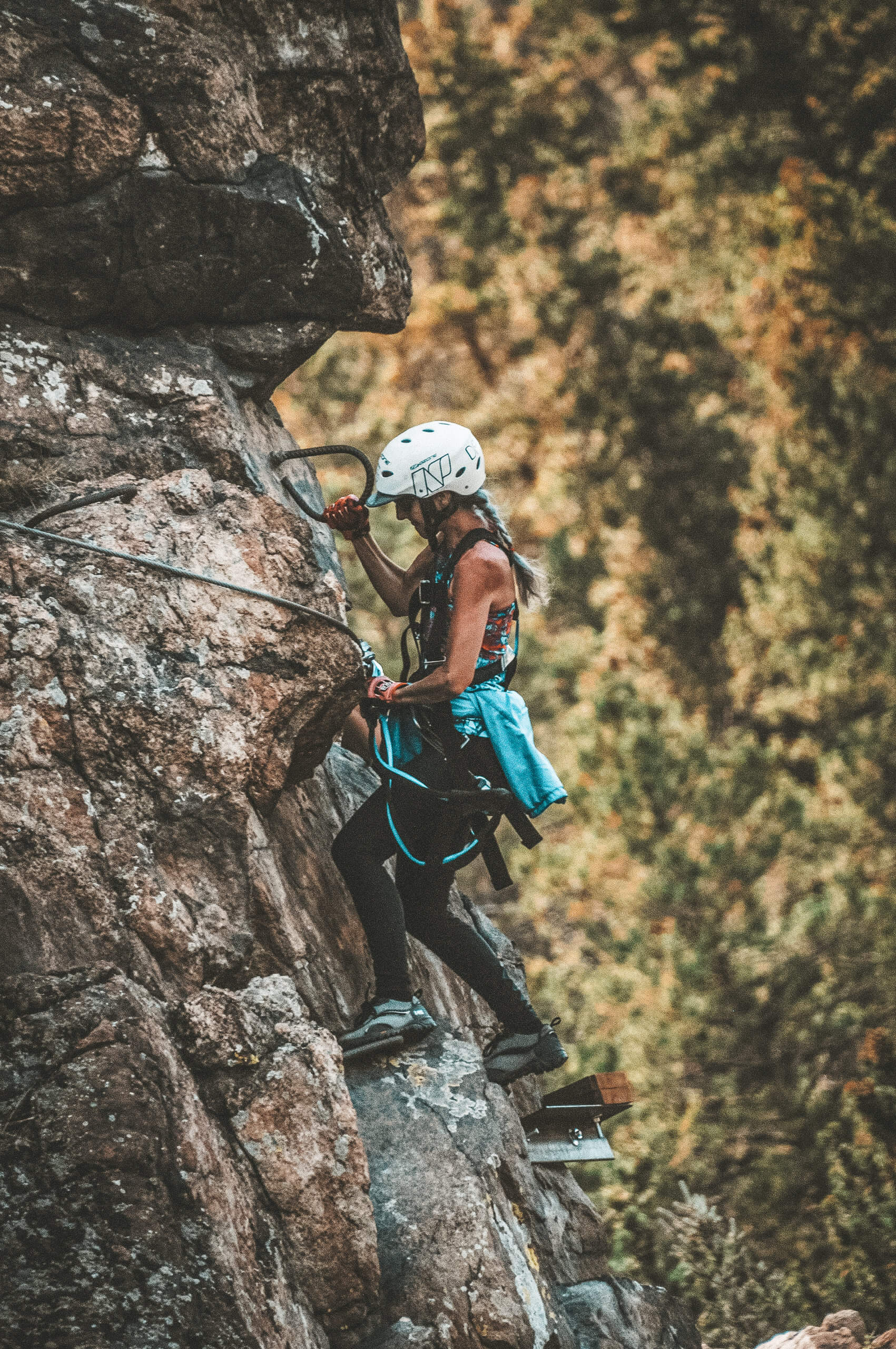 Woman on the Granite Via Ferrata about to go around the cliffside suspended by iron rungs with a mountain face in the background