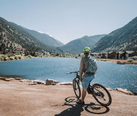 A man sitting on a bike with a backpack in front of a lake in Colorado