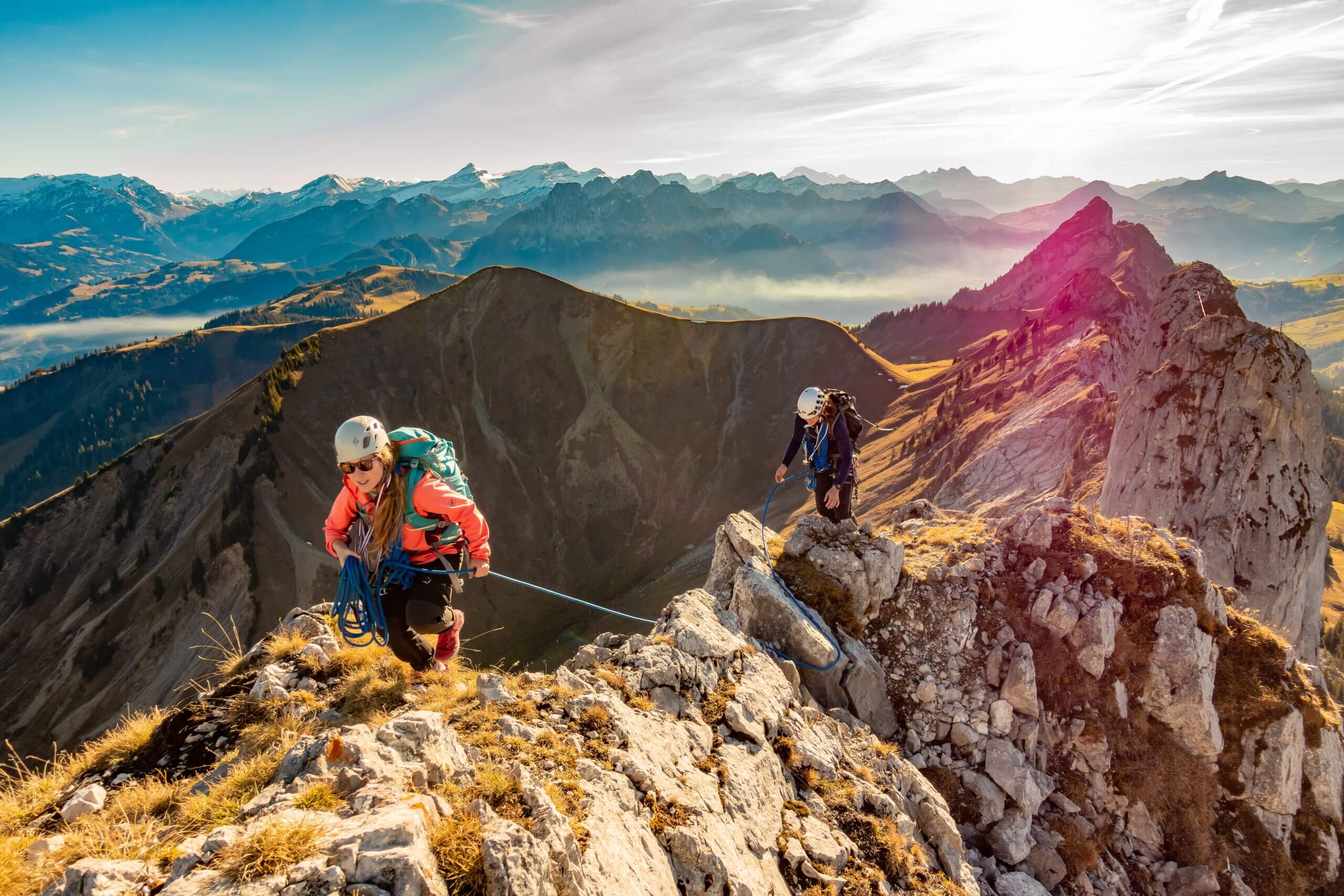 two woman climbing across mountaintop